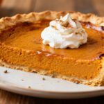 Air fryer pumpkin pie with a flaky golden pie crust, smooth creamy pumpkin filling, whipped cream, and a sprinkle of pumpkin pie spice, served as a classic fall dessert.