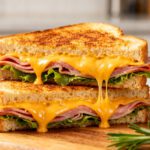 Air fryer hot ham and cheese sandwich with crispy golden toasted bread, savory sliced ham, gooey melted cheddar cheese, fresh lettuce, and steam rising, served as a warm comfort food meal.