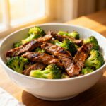 Air fryer beef and broccoli with tender sliced beef, roasted broccoli florets, savory glossy sauce, and sesame seeds, served as an easy high protein weeknight dinner.
