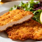 Air fryer chicken schnitzel with crispy golden panko breading, juicy tender chicken breast, fresh mixed greens, and lemon wedges, served as an easy comforting dinner.