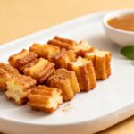 Air fryer churro bites with crispy golden churro pieces coated in cinnamon sugar, a soft fluffy interior, and caramel dipping sauce, served as an easy homemade dessert.
