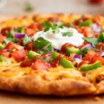 Air fryer Mexican pizza with a crispy golden crust, seasoned taco beef, melted cheddar cheese, diced tomatoes, green peppers, red onions, sour cream, and fresh cilantro, served as an easy Tex Mex dinner.