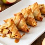 Air fryer caramel apple wontons with crispy golden wonton wrappers, warm cinnamon apples, rich caramel drizzle, and a flaky crunchy texture, served as an easy fall dessert.