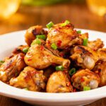 Air fryer chicken gizzards with crispy caramelized chicken gizzards, sliced green onions, red chili peppers, and savory seasoning, served as a flavorful high protein appetizer or main dish.