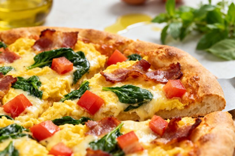 Air fryer breakfast pizza with fluffy scrambled eggs, crispy bacon, fresh spinach, diced tomatoes, melted cheese, and a golden pizza crust, served as a hearty homemade breakfast.
