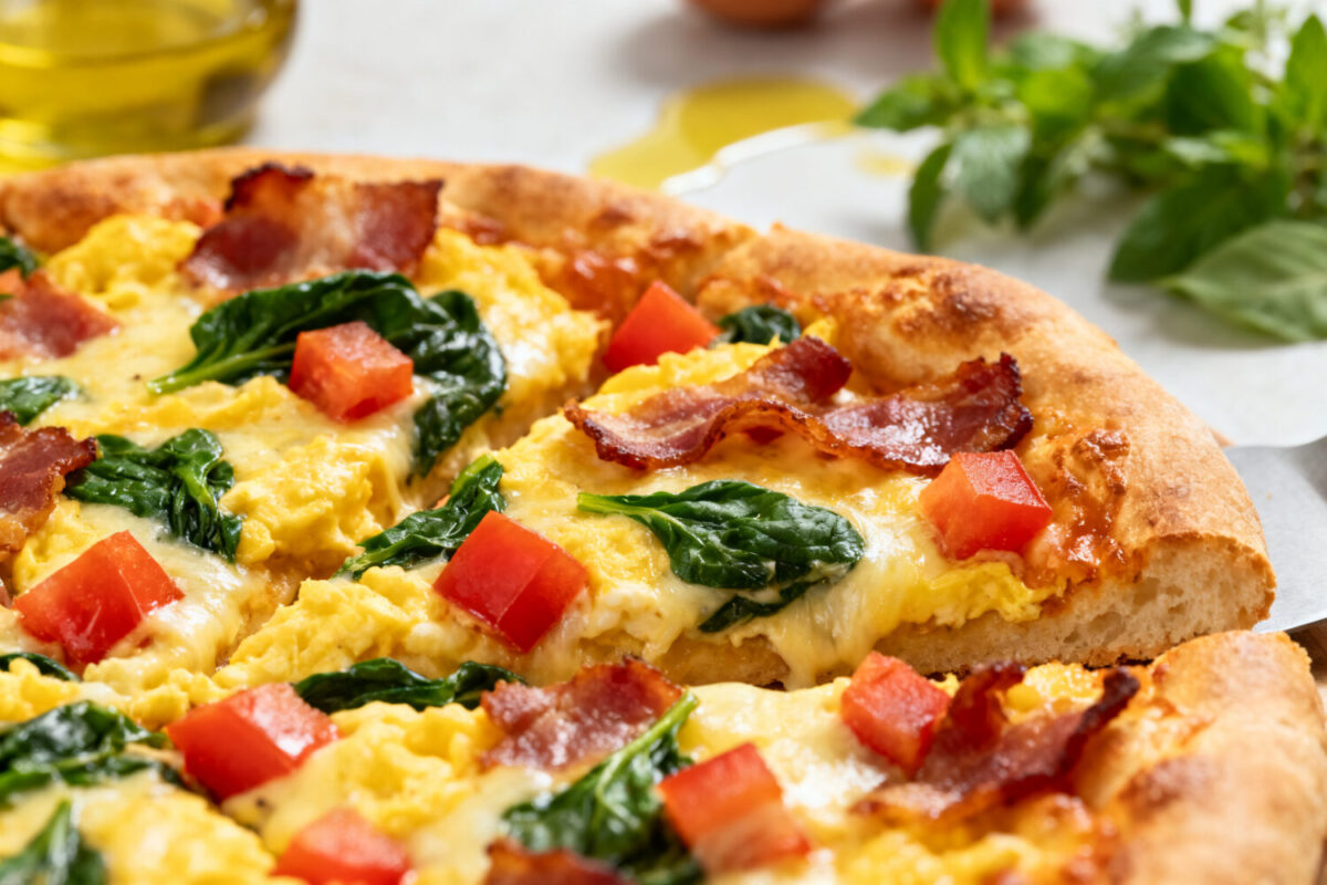 Air fryer breakfast pizza with fluffy scrambled eggs, crispy bacon, fresh spinach, diced tomatoes, melted cheese, and a golden pizza crust, served as a hearty homemade breakfast.