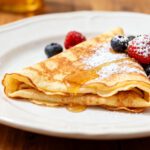 Air fryer crepes with thin tender golden crepes, powdered sugar, maple syrup, fresh strawberries, raspberries, blueberries, and blackberries, served as an easy homemade breakfast.
