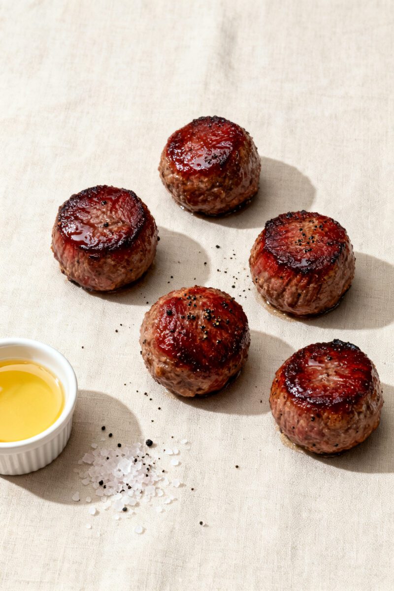 5-inch spheres showing deep mahogany sear and moist sheen; a tiny ramekin of melted butter/tallow fo