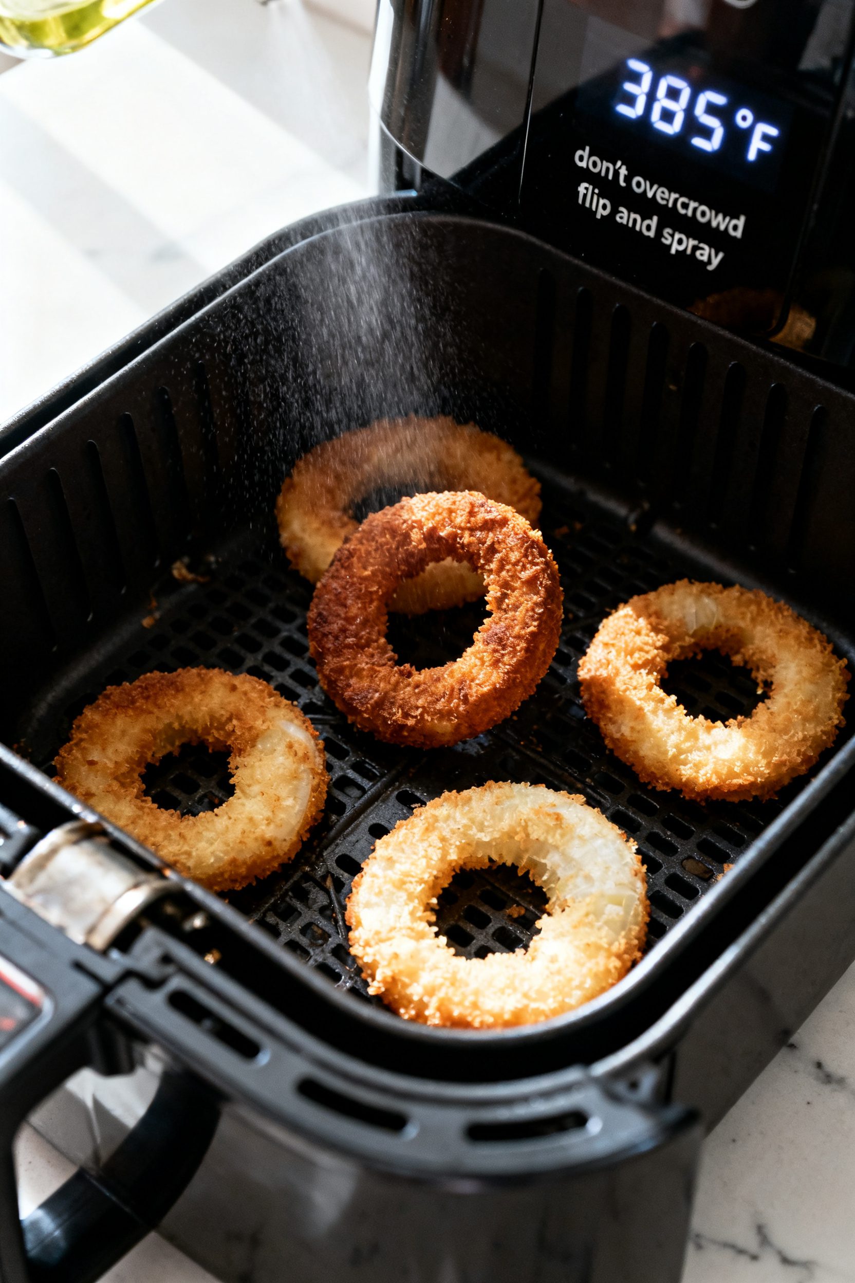 Cooking process: Air fryer basket shot at midway flip—single layer of breaded onion rings spaced a