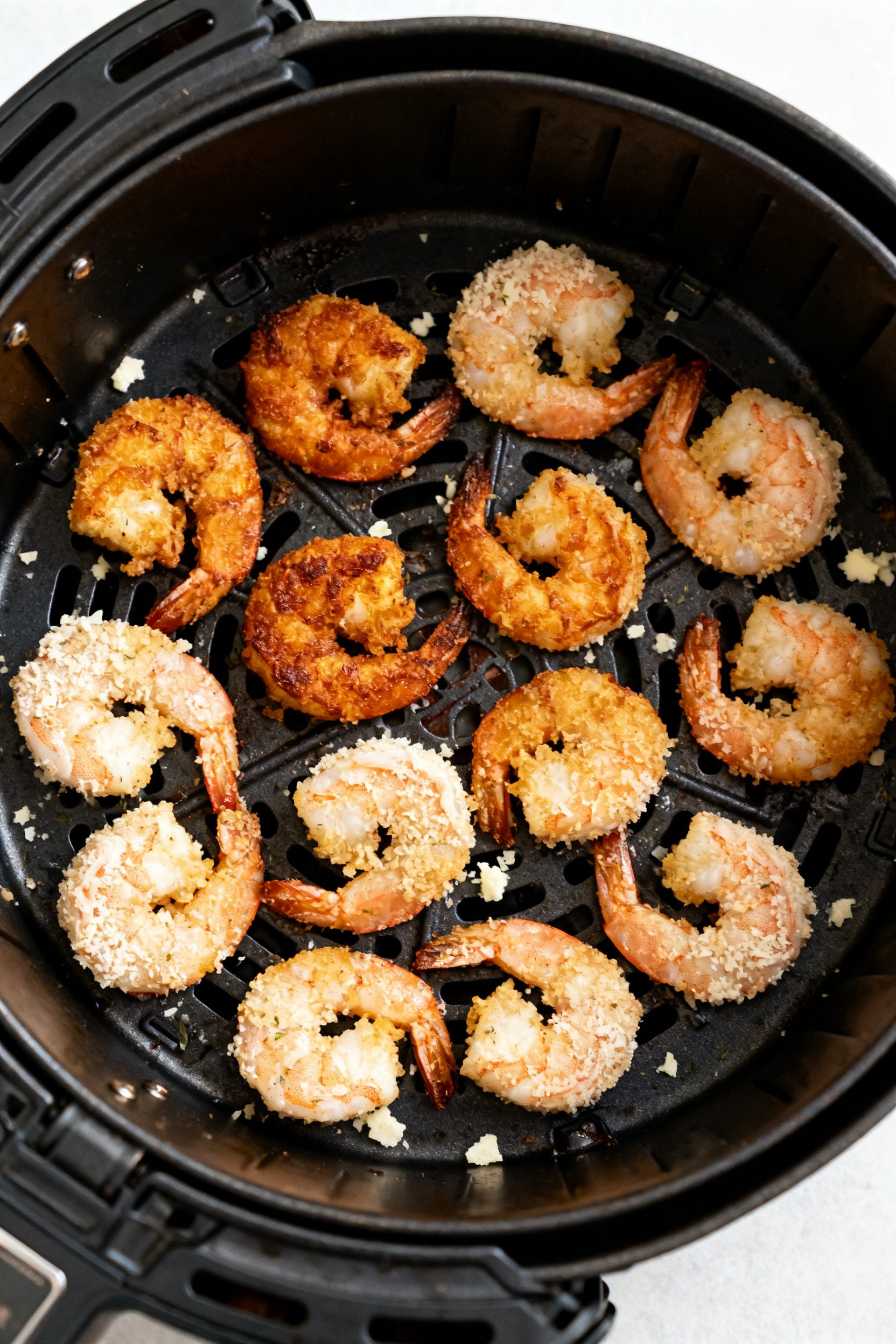 Cooking process: Overhead shot of a single-layer arrangement of coated shrimp in an air fryer basket