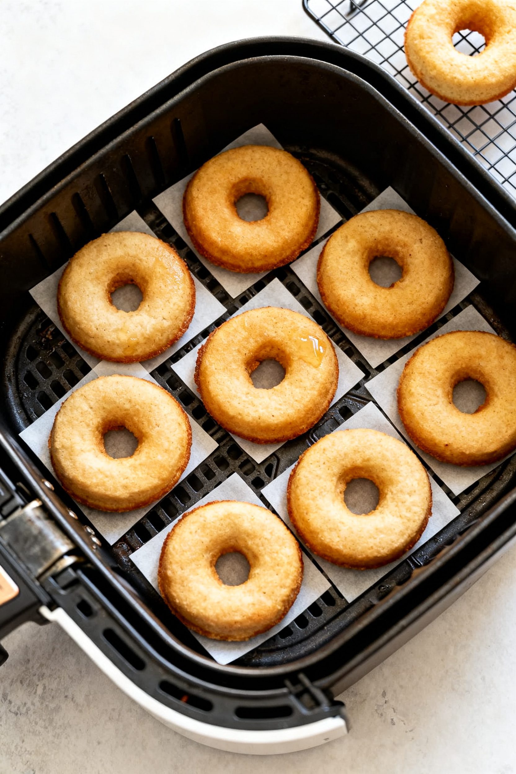 Cooking process: Overhead shot of an air fryer basket lined with small parchment squares, evenly spa