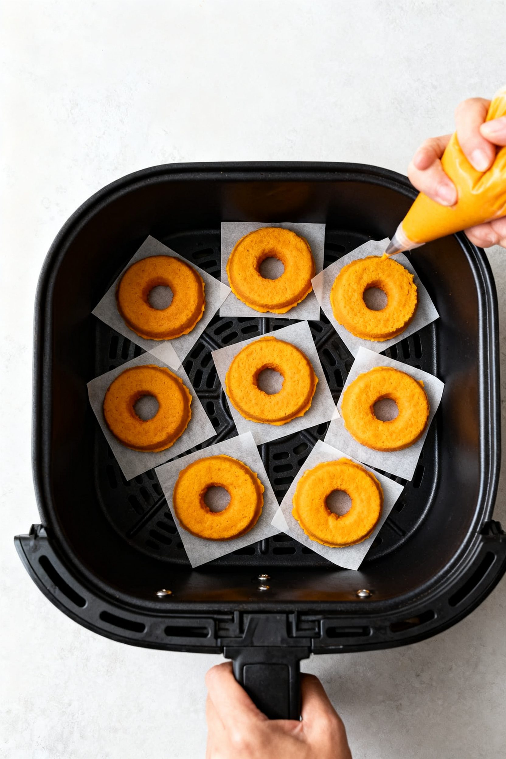 Cooking process: Overhead shot of piped pumpkin donut rings on individual parchment squares being pl