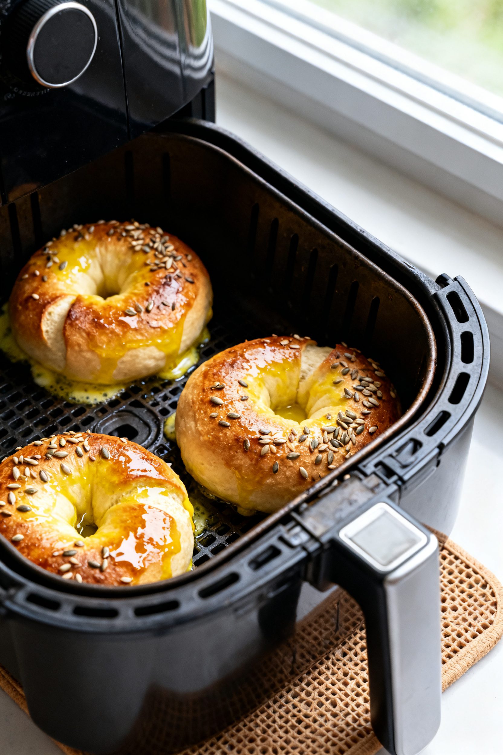 Cooking process shot: Air fryer basket scene with three shaped, egg-washed keto bagels mid-cook at 3