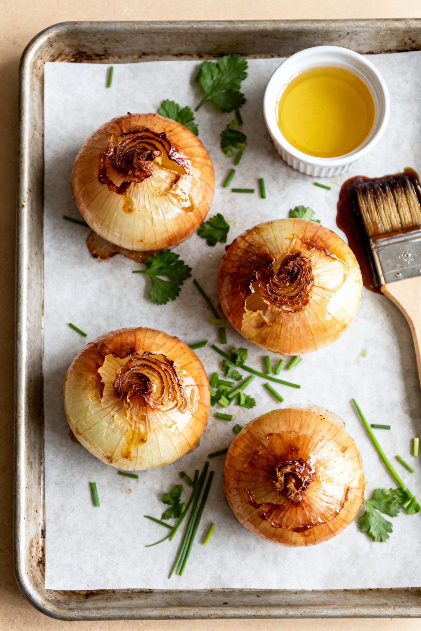 Overhead “tasty top view” of four cooked whole onions resting on a parchment-lined tray: evenly 